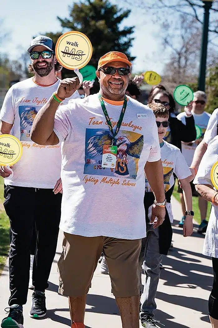 Darrin Johnson walks, holding an orange "Walk MS" sign