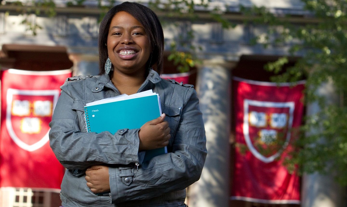 Imani, a woman with MS, holding notebooks while standing in front of a college building
