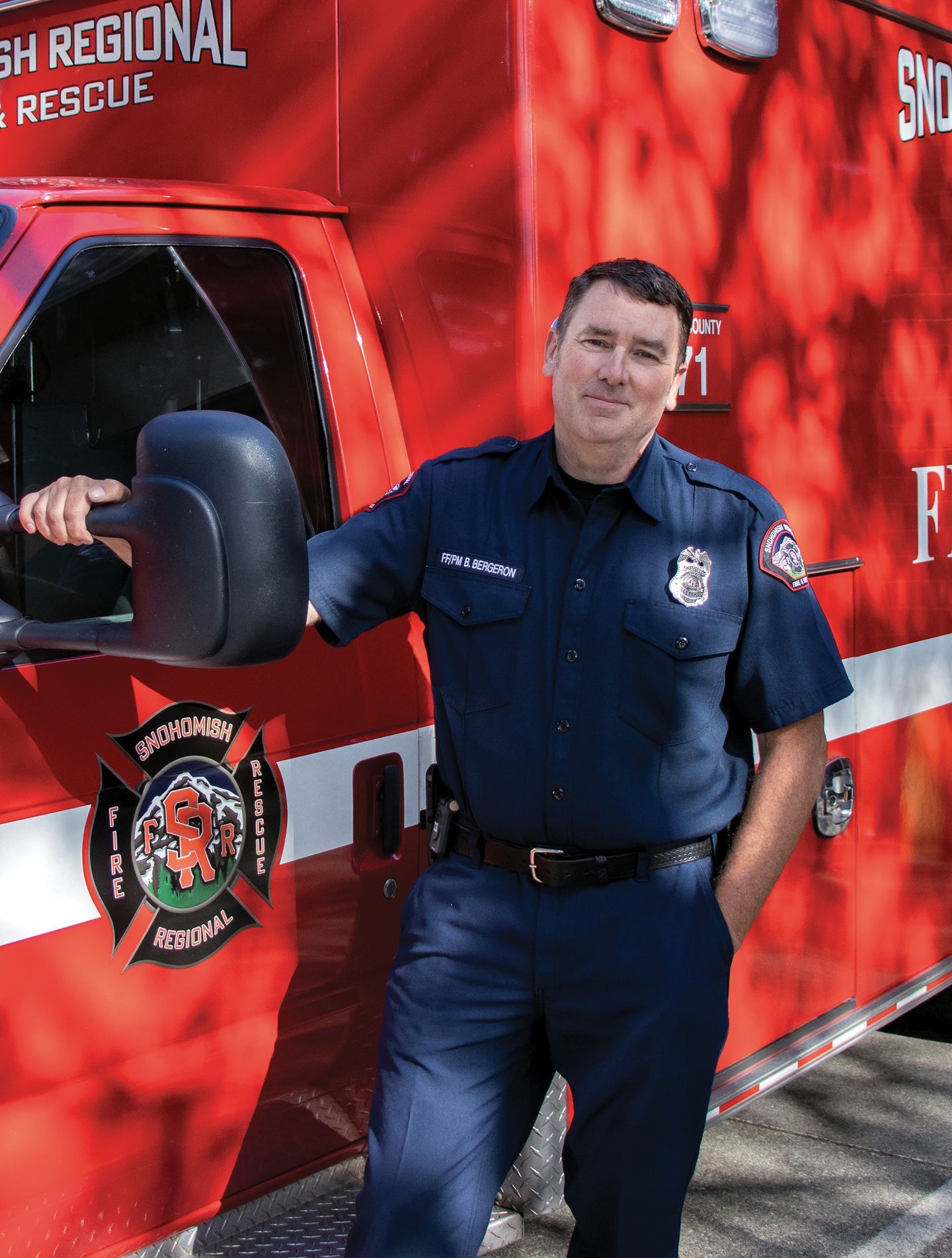 A man in a firefighter/paramedic uniform stands in front of a fire & rescue truck.