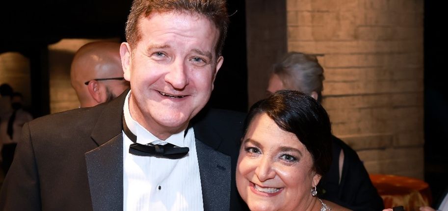 A man in a black tuxedo and a woman in a black dress smile together.