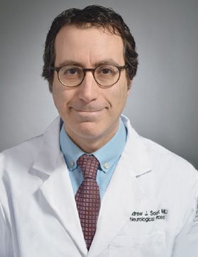Andrew Solomon, MD, wears glasses, a tie, and a lab coat bearing his name and title