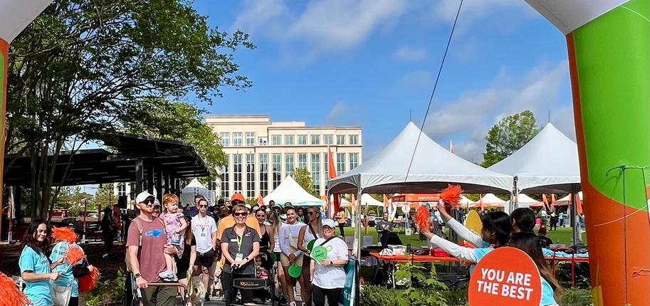 A crowd of people gather at a Walk MS starting line arch that reads "Let's Go!"