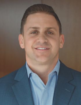 A white man with short, brown hair wearing a blue jacket and light blue shirt.