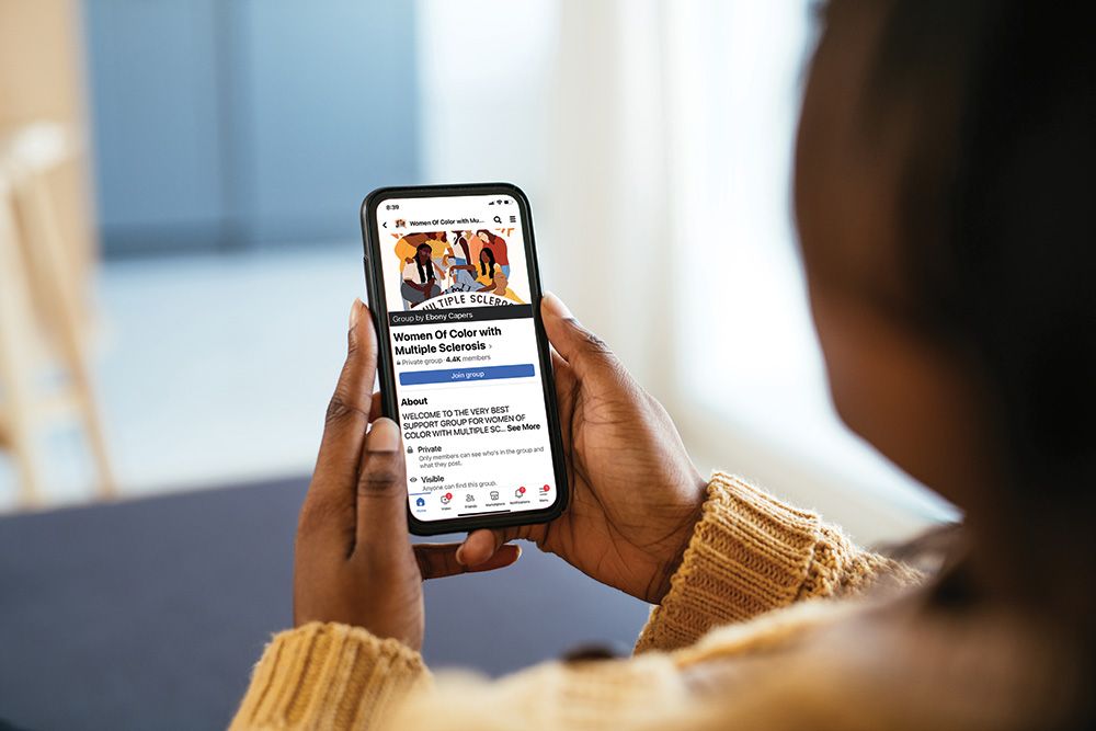 A woman holds a mobile phone that displays the Women of Color With Multiple Sclerosis Facebook group