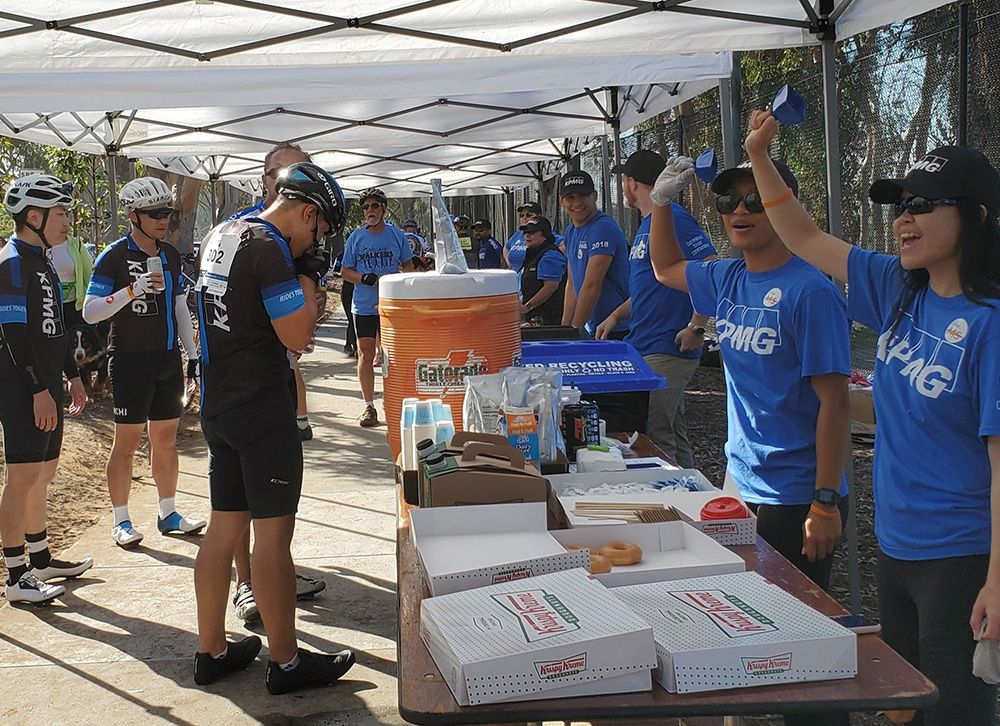 Cyclists make a stop at a rest stop as KPMG volunteers ring cowbells.