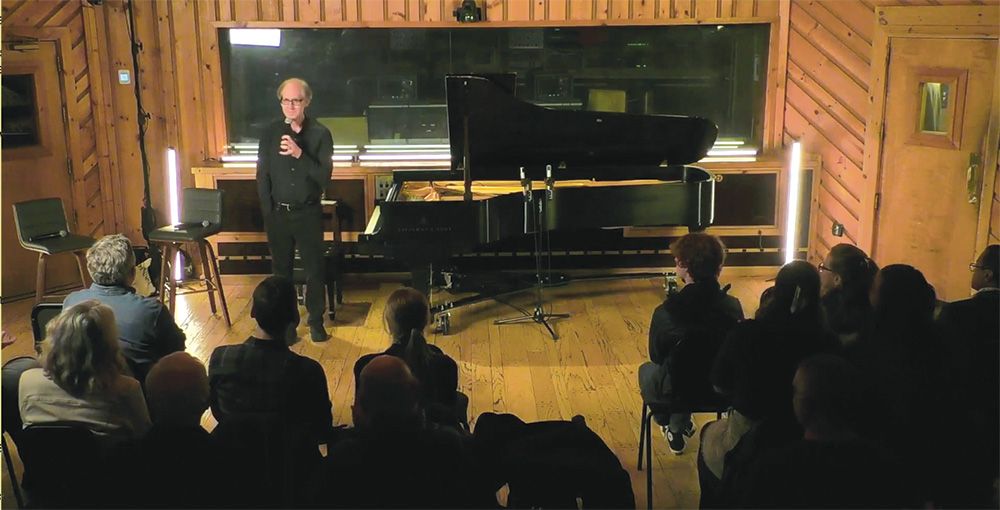 Jeff Beal stands by a grand piano in a recording studio, in front of a small audience.