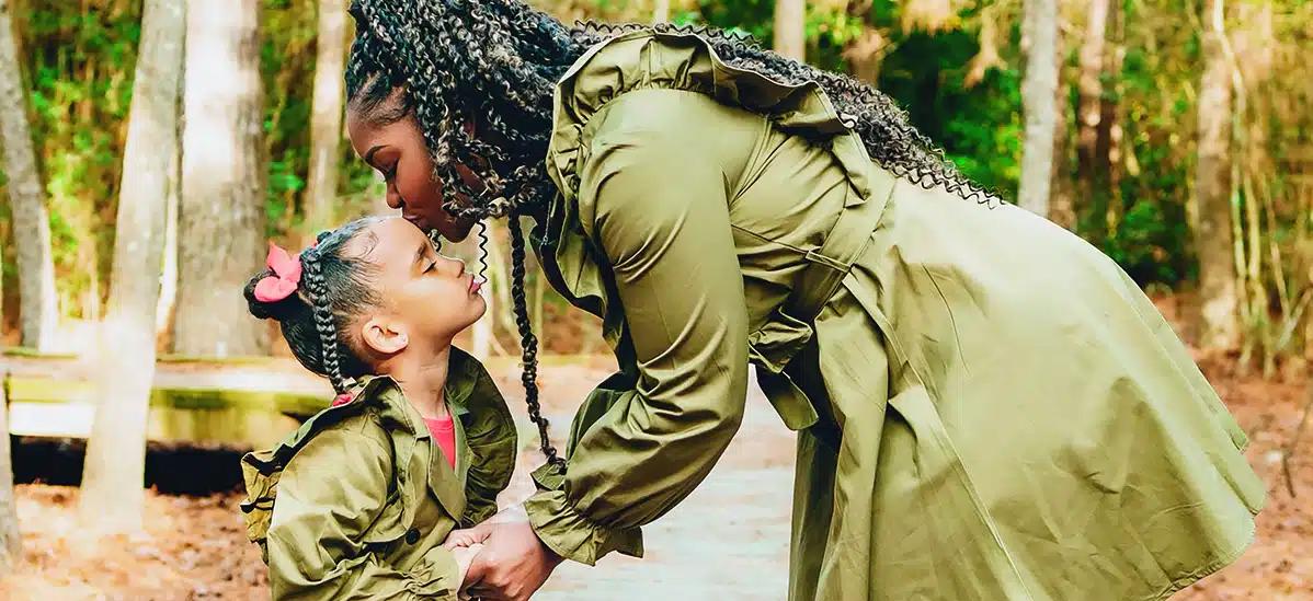Shabanese Barrick leans down and kisses her daughter on the forehead. The two are wearing matching green jackets.