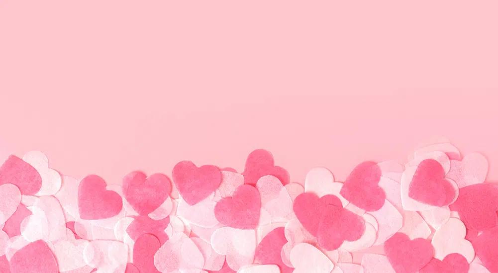 A pile of white and pink, heart-shaped confetti on a pink background. 