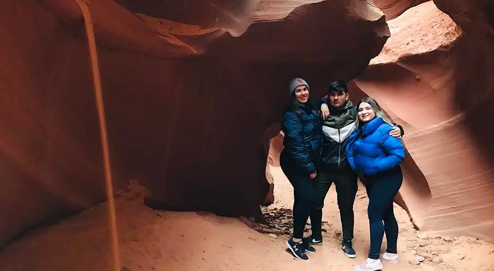 Two women and one man stand posed for a photo in a cave
