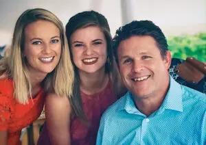 From left to right, a white woman with blonde hair in orange top, a white woman with brown hair in purple shirt, and white man with blue shirt all smiling at the camera.