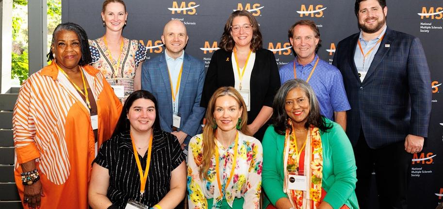 A group of men and women pose for a photo in front of a National Multiple Sclerosis Society black backdrop.