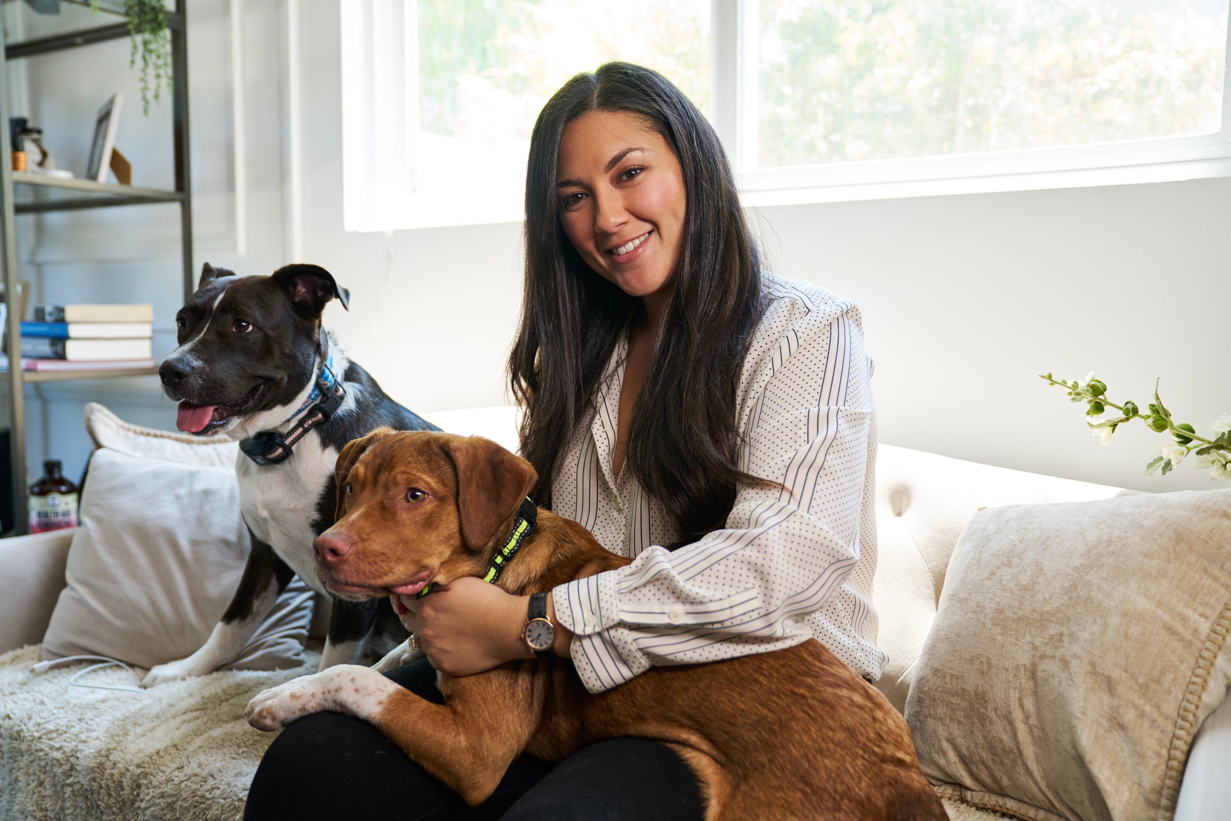 A woman poses with two dogs on a couch