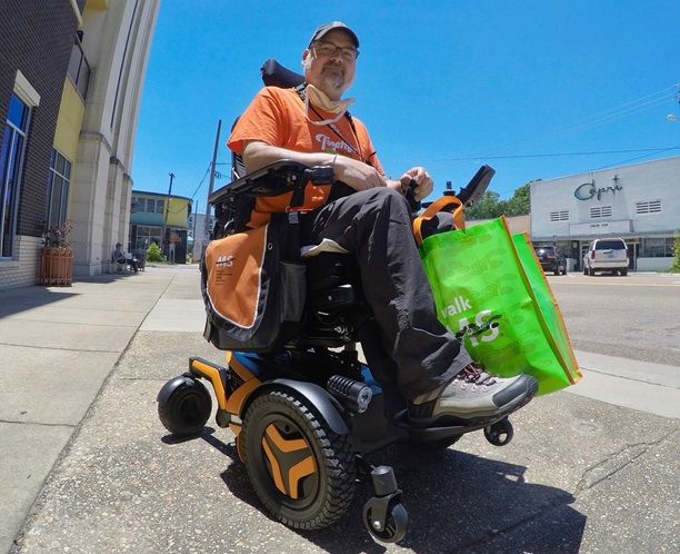 Scott Crawford sits in a mobility scooter with orange trim wearing an orange shirt.