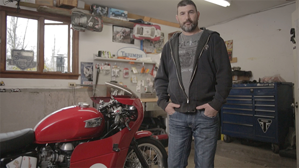 Dave, diagnosed with MS, standing in a garage next to a red motorcycle.