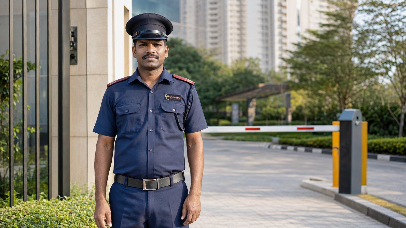 Whitehand security guard on duty at a Bangalore gated-community entrance gate with a boom barrier