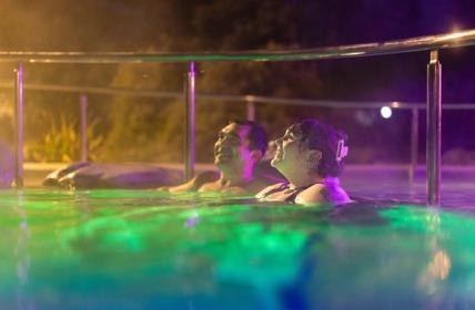 Couple relaxed against the walls with the beautiful Rainbow pools lights around them at night at Hanmer Springs