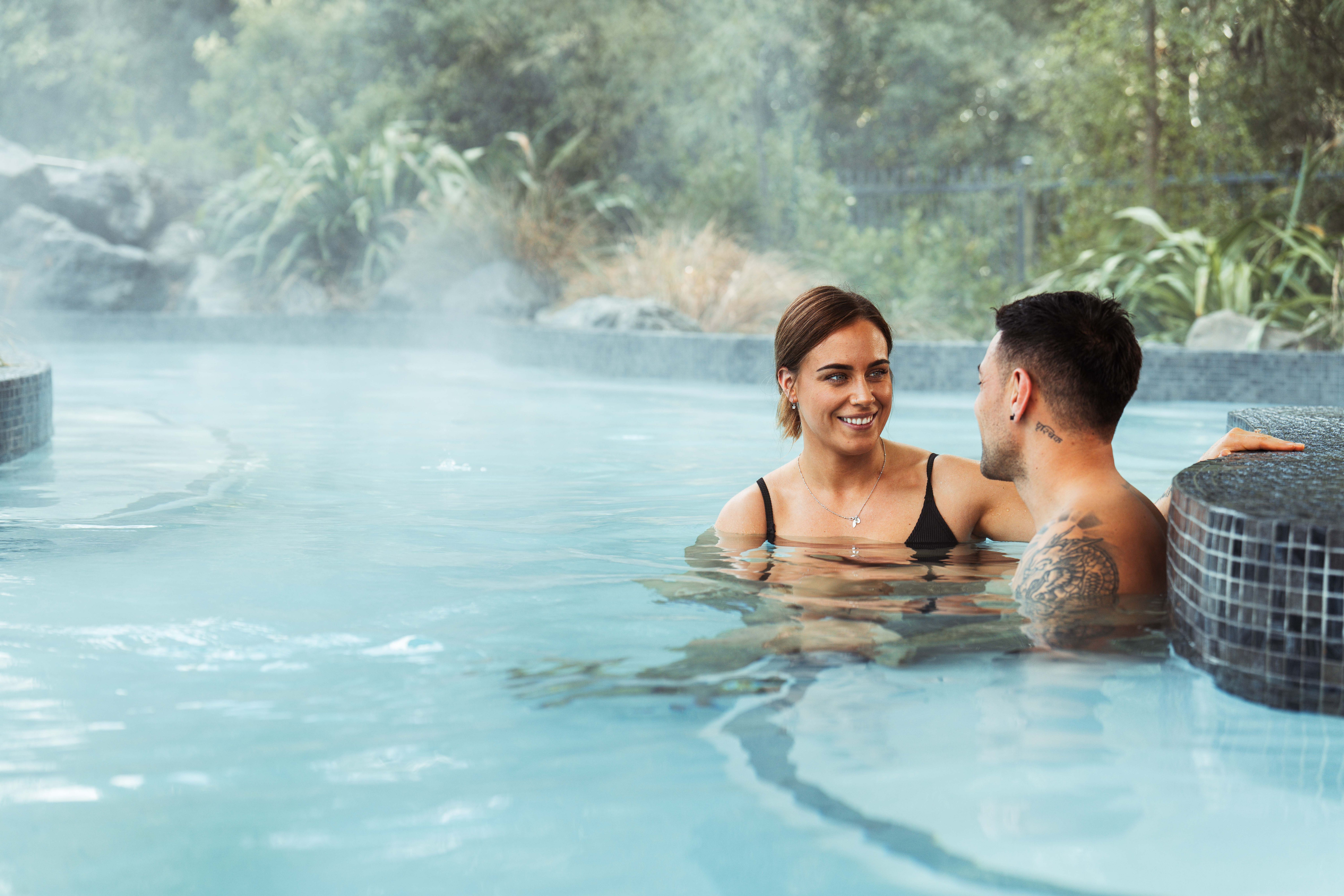 A young couple sit in the Hanmer Springs Thermal Pools and Spa. They look at each other. 