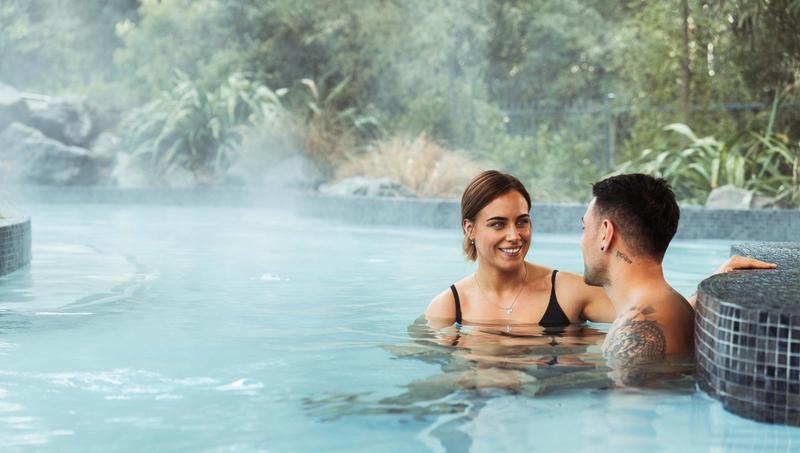 A young couple sit in the Hanmer Springs Thermal Pools and Spa. They look at each other.