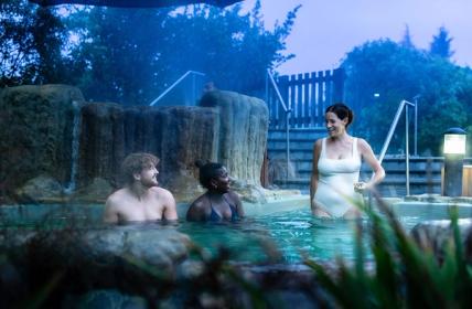 Three friends chat in one of the thermal pools with steam rising around them