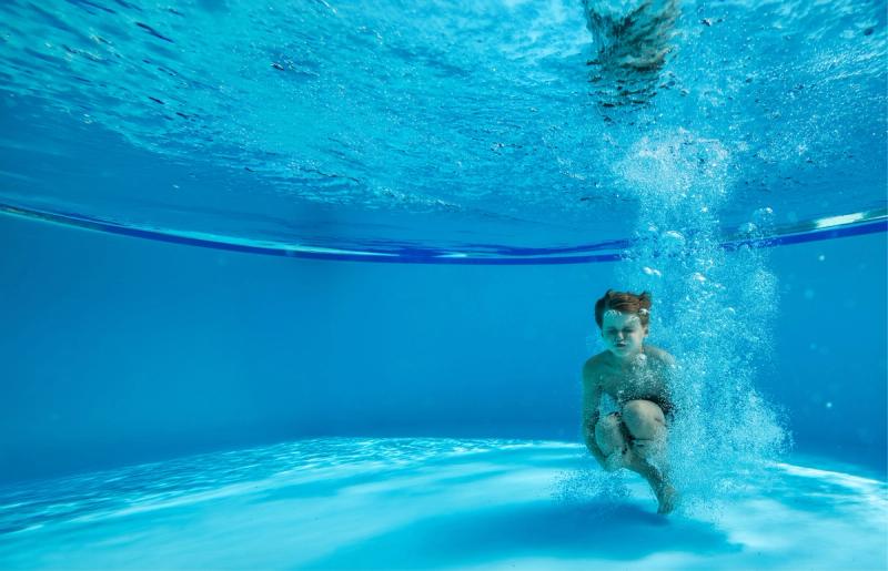 A young boy underwater after jumping in the pool with bubbles all around him