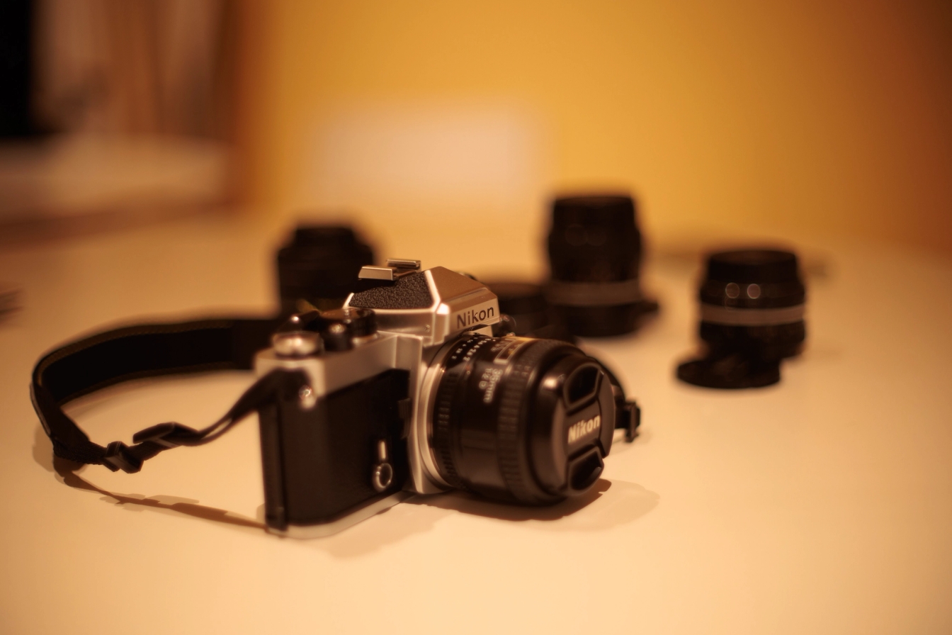 A picture of a Nikon FE film camera on a table. The background is highly blurred.