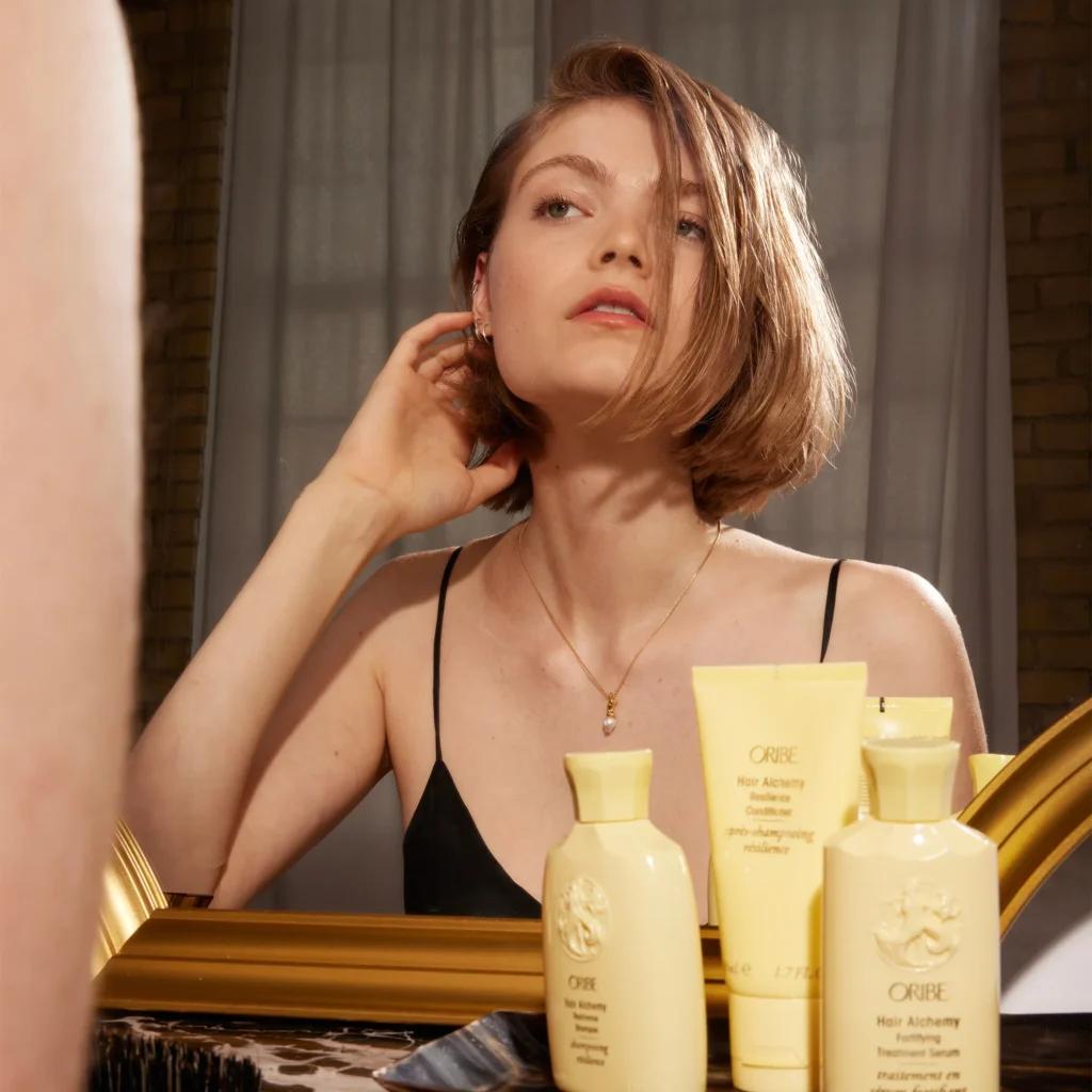 model with healthy hair posing alongside the oribe alchemy collection
