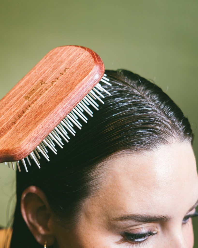 Close-up of a woman brushing her wet hair with the Fabio Scalia La Claudia paddle brush, stimulating the scalp and evenly distributing treatment for optimal scalp health and shine.