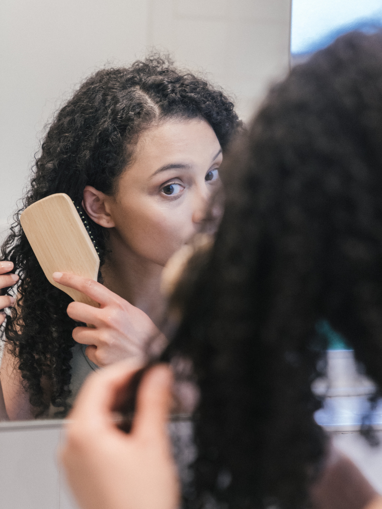 Curly-haired model brushing hair and checking for dryness, highlighting challenges of low porosity curls