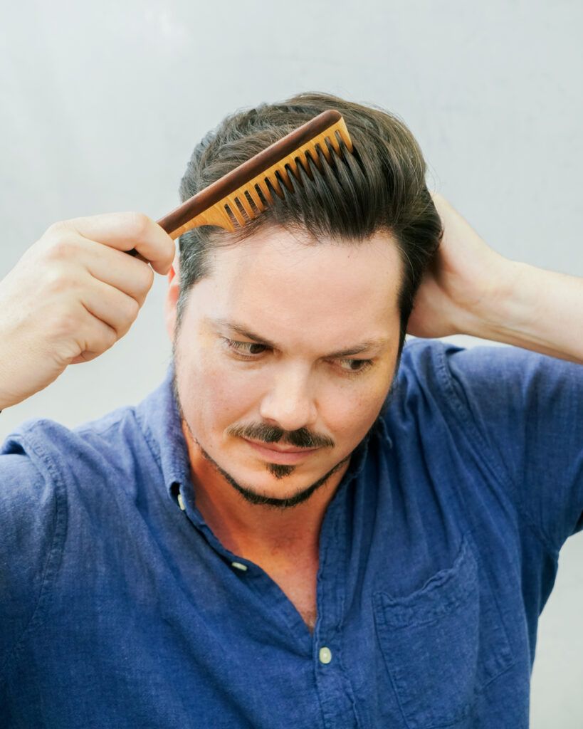 Man styling his hair with a Leo wooden comb, gently combing through the top of his hair to shape and add lift, showcasing the comb’s wide teeth and natural wood grain.
