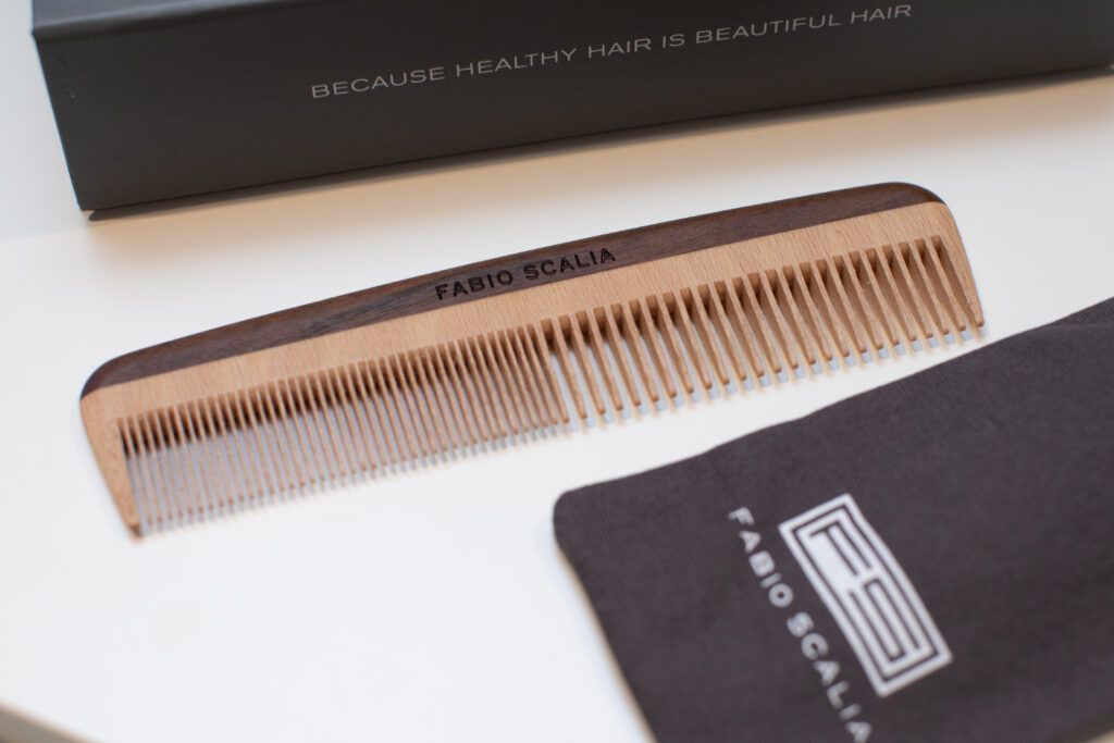 Close-up of the Fede wooden comb by Fabio Scalia, featuring dual-tone beech and walnut wood with fine teeth, shown with its branded pouch and box reading “Because healthy hair is beautiful hair"