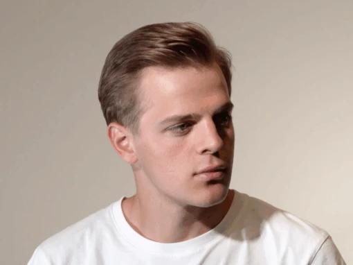 Man with neatly styled slicked-back hair wearing a white shirt, showcasing a polished men’s blowout with a smooth finish and subtle volume.