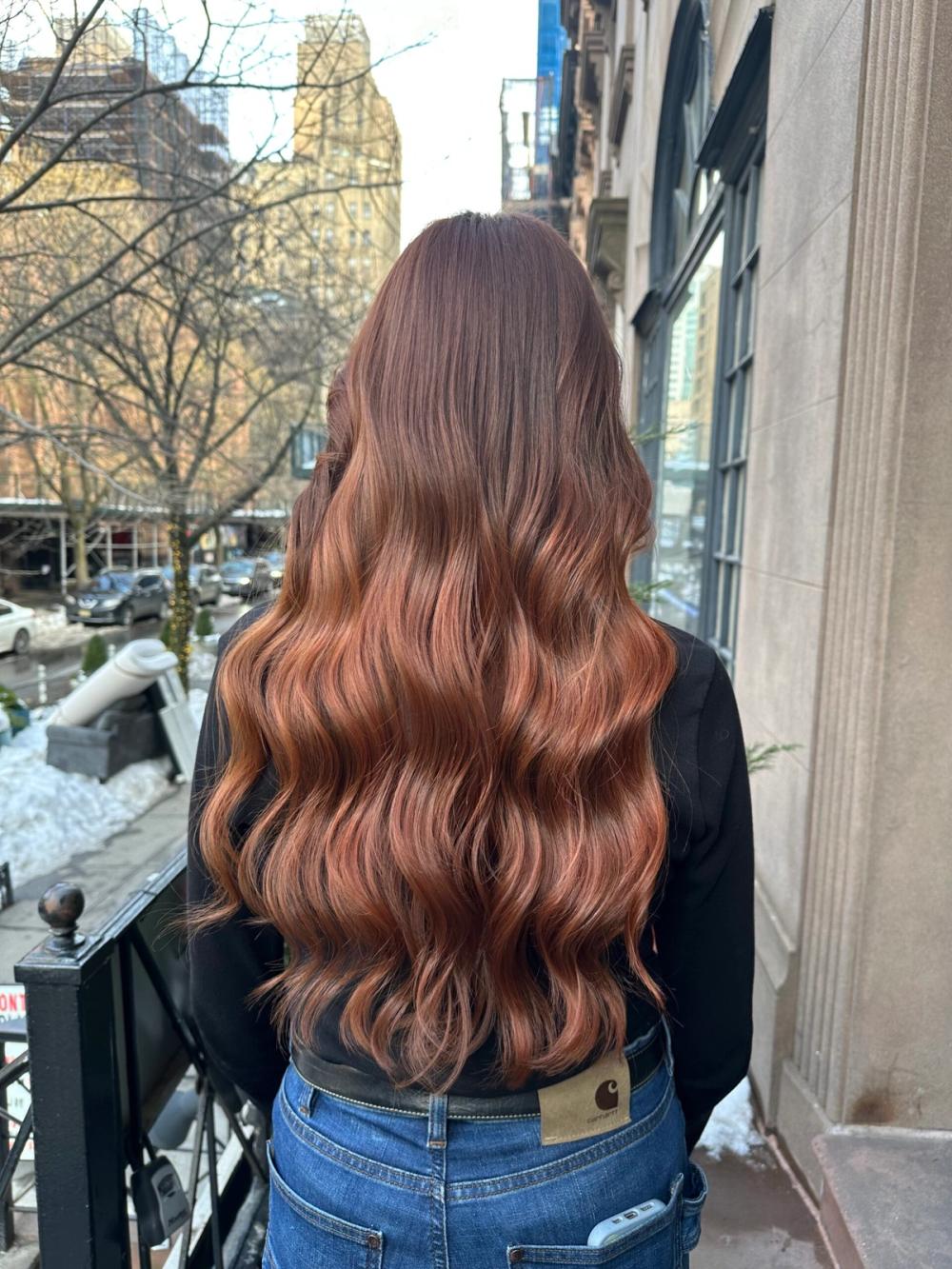 Long brunette hair with soft, flowing waves and warm copper balayage, styled with a glossy, dimensional finish.