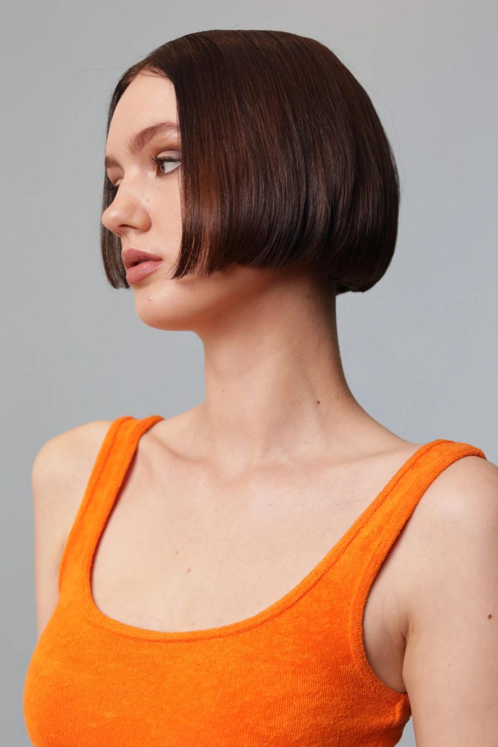 Model with a sleek jaw-length blunt bob and glossy auburn brunette color, styled with a precise, polished finish.