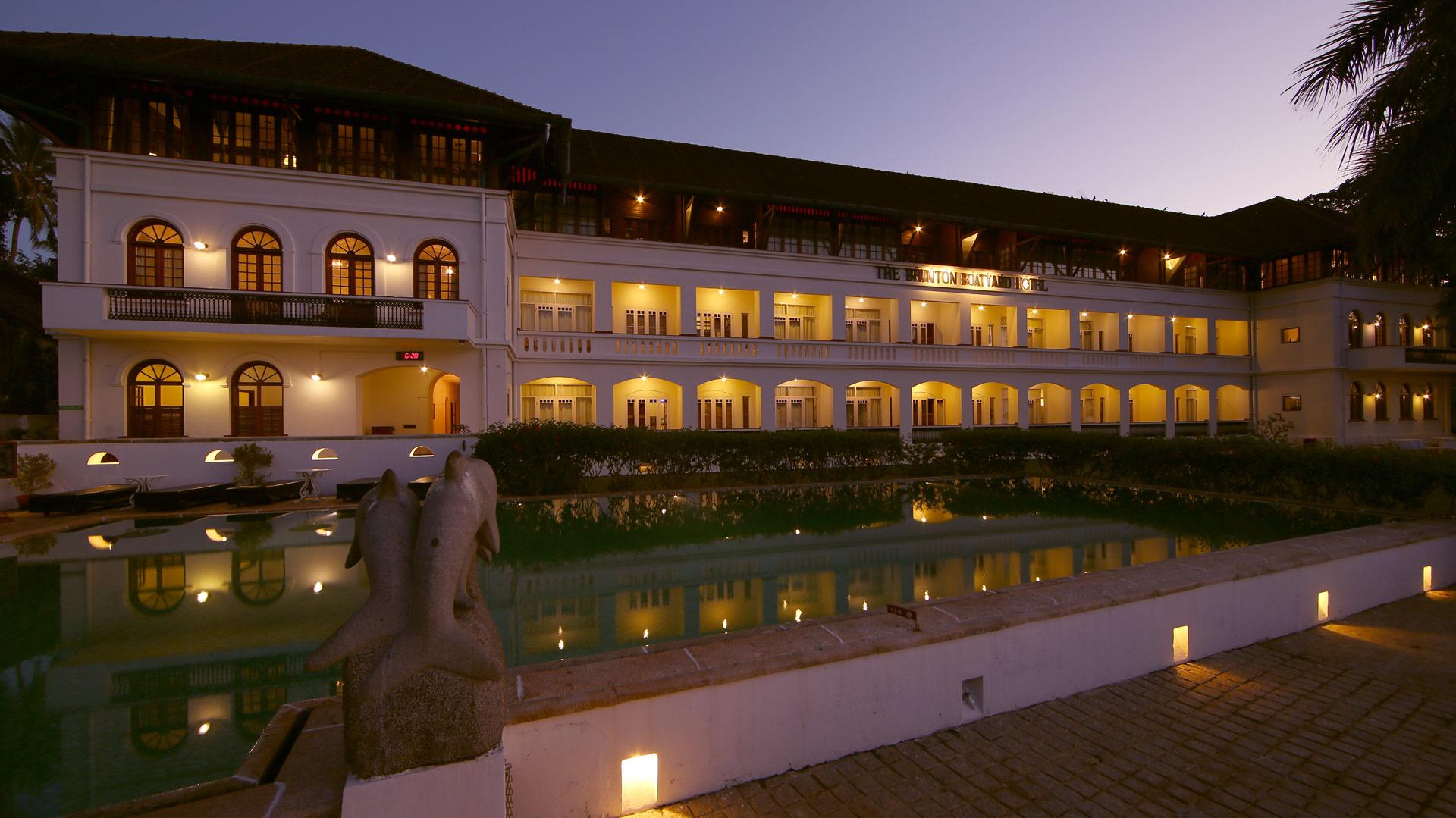The hotel's white building lit up at dusk behind an ornamental pool with a carved dolphin statue, its name lettered across the upper storey.
