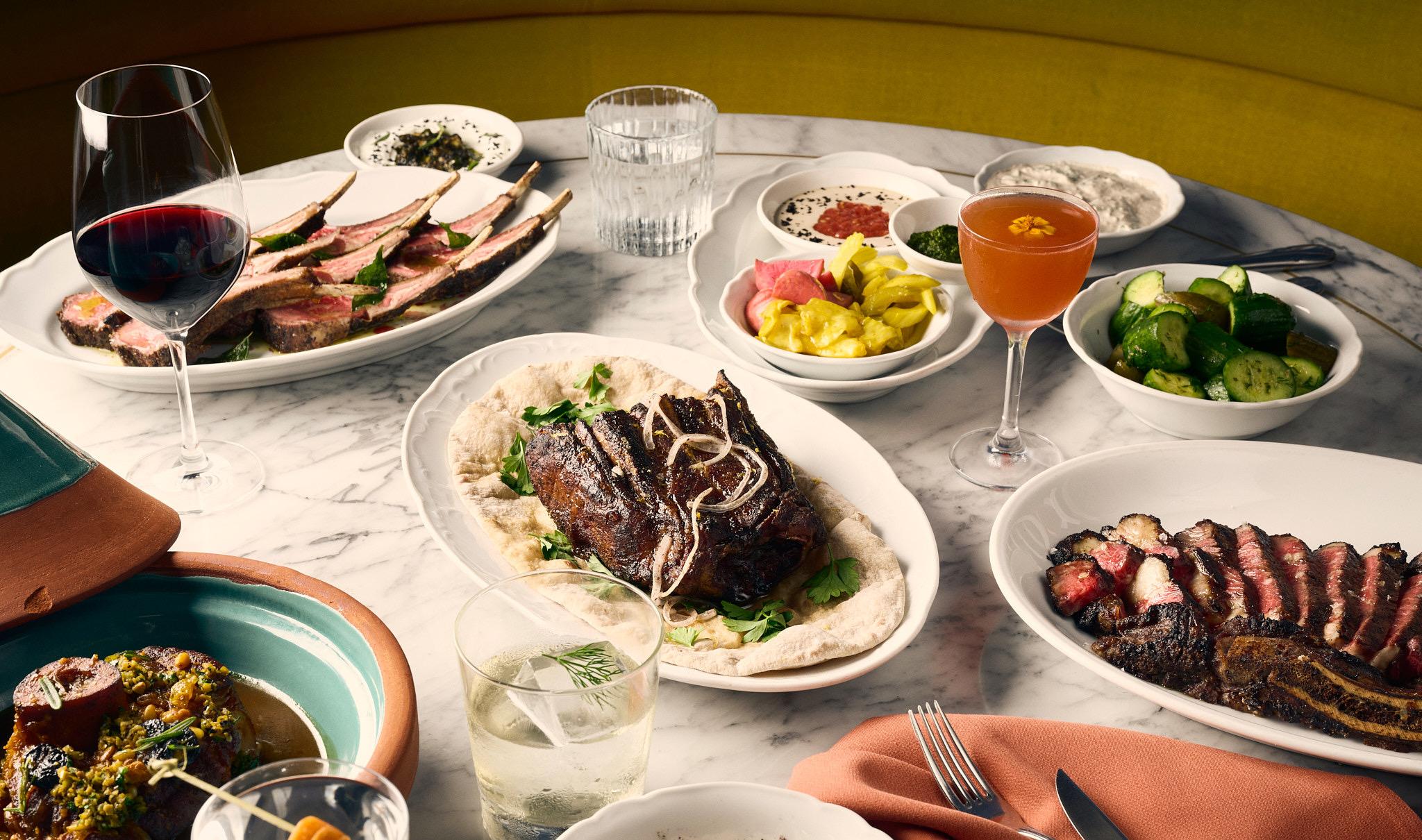A table at Bavel laid with grilled meat, dips, salads and cocktails, seen from above