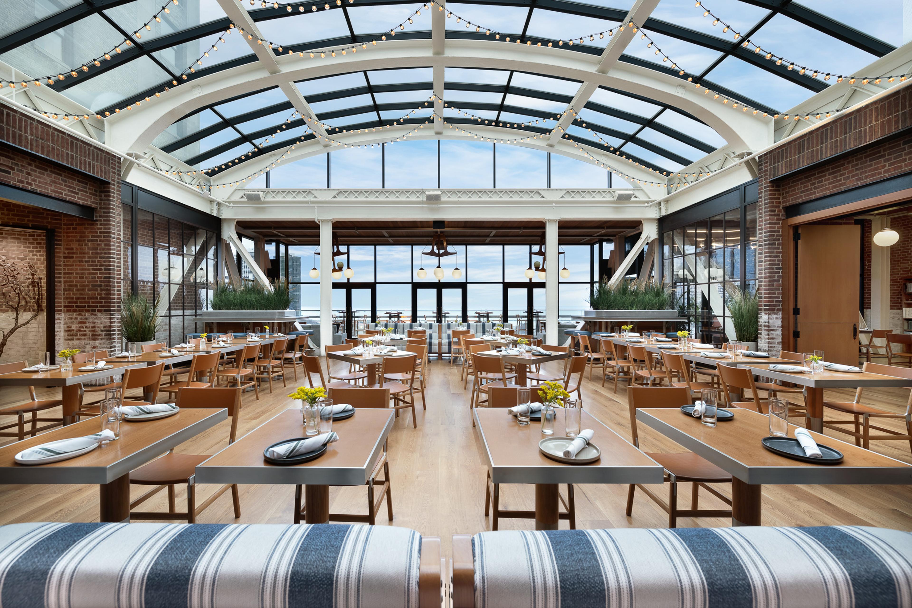 Long tables under the arched glass roof of the rooftop restaurant, with the sky beyond