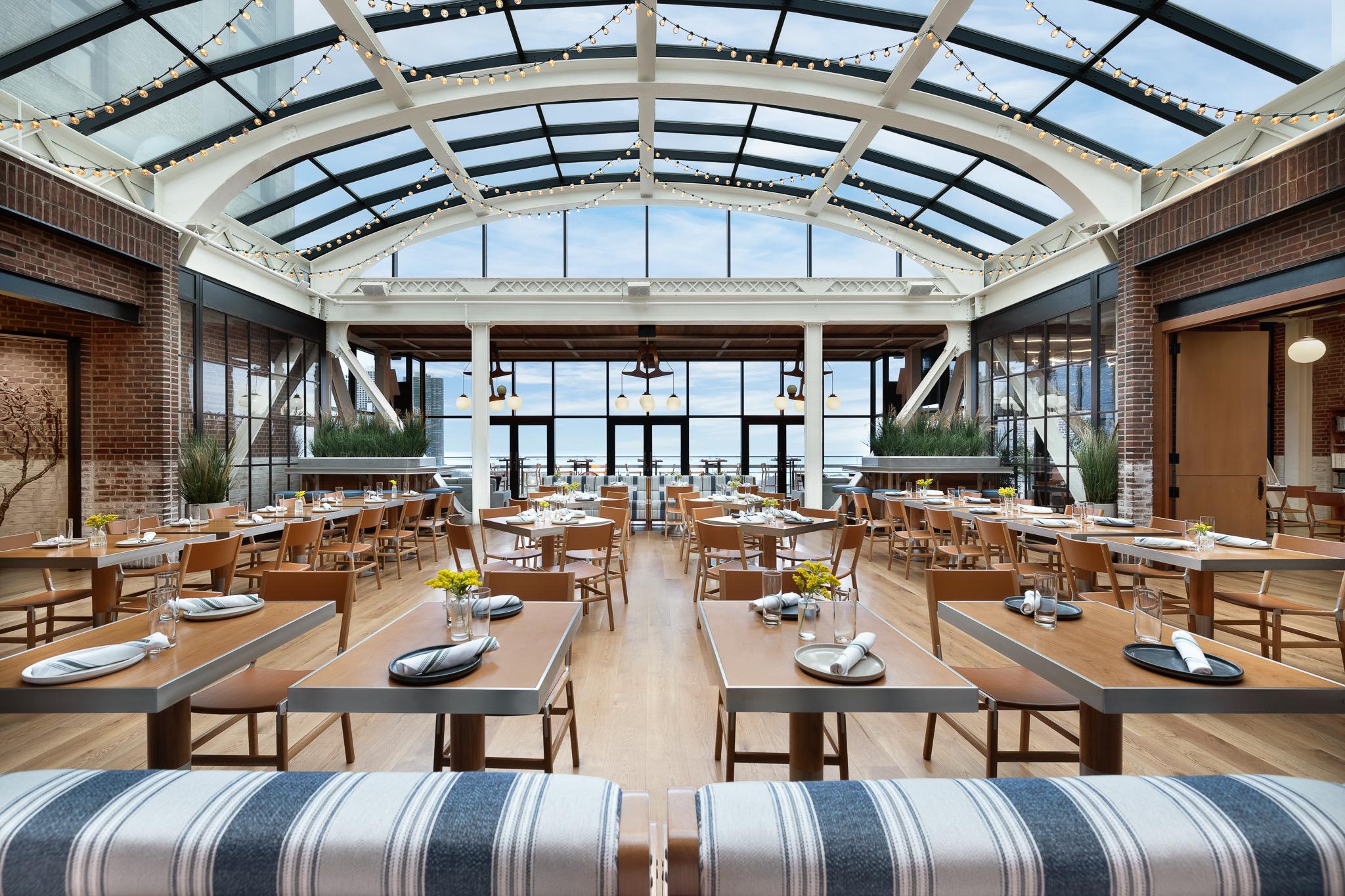 Long tables under the arched glass roof of the rooftop restaurant, with the sky beyond