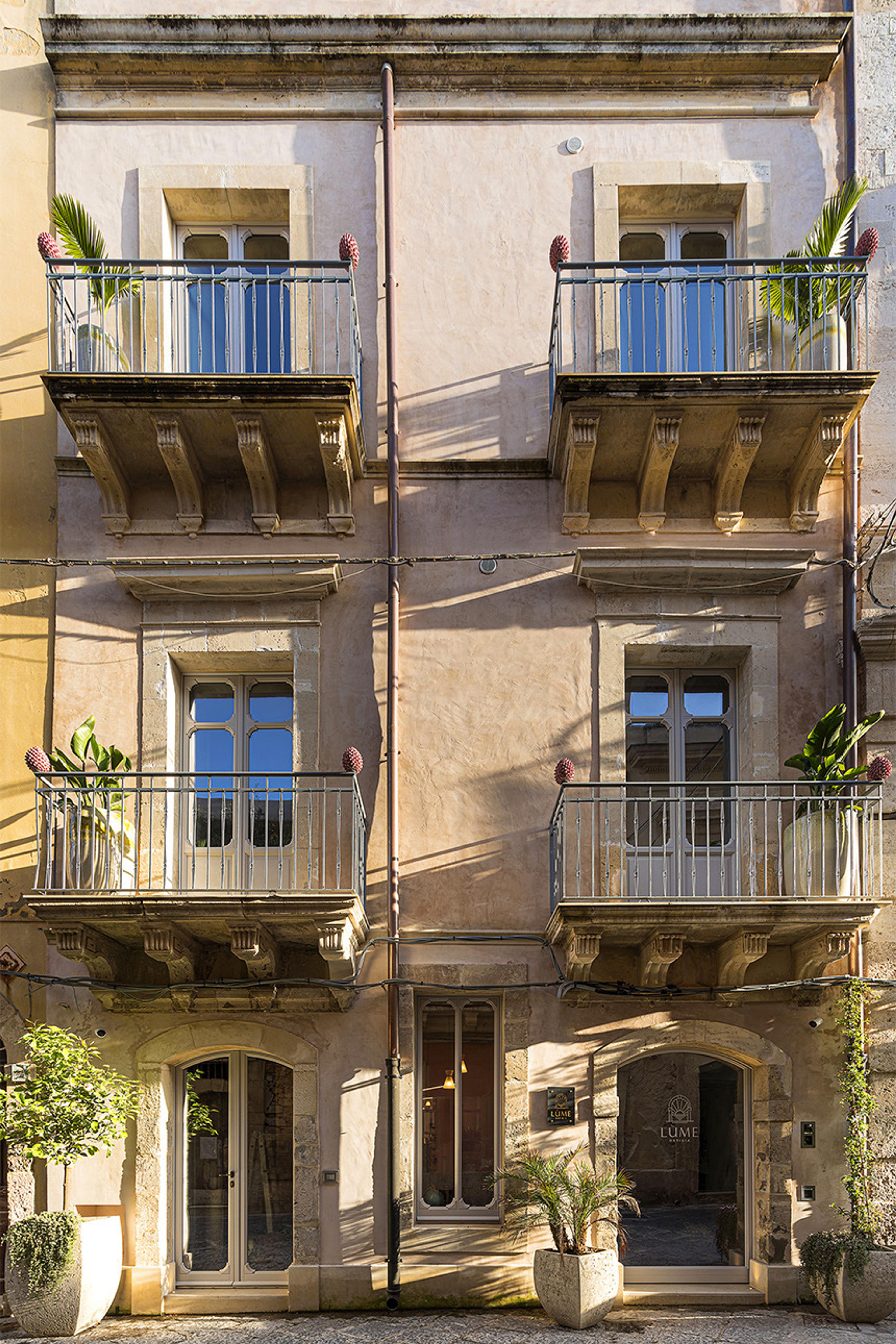 The cream stone facade of a four storey building with wrought iron balconies, potted plants and a ground floor entrance marked Lume.