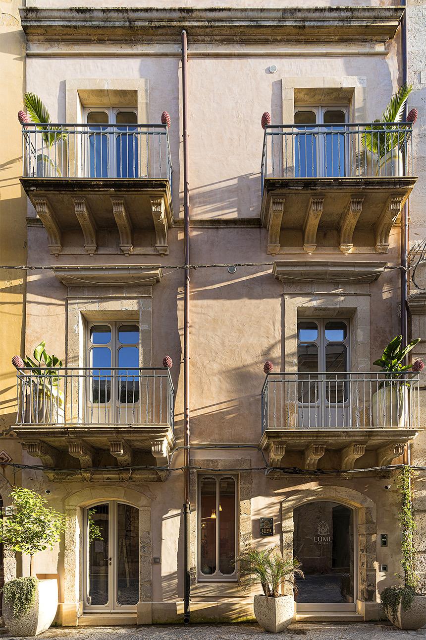 The cream stone facade of a four storey building with wrought iron balconies, potted plants and a ground floor entrance marked Lume.