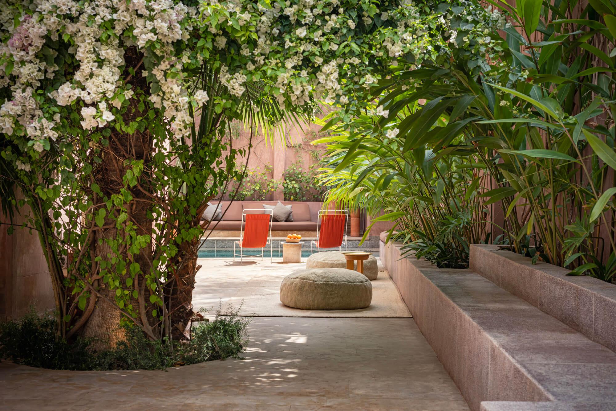 a terrace with red lounge chairs and a cushioned bench beside a pool, framed by a flowering bougainvillea and palm fronds