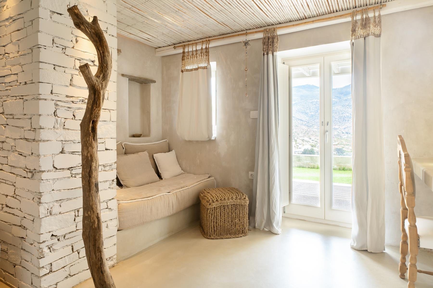 A living room with a driftwood post and a stone pillar, a daybed under a bamboo ceiling, and a glass door looking out to a lawn and a mountain.
