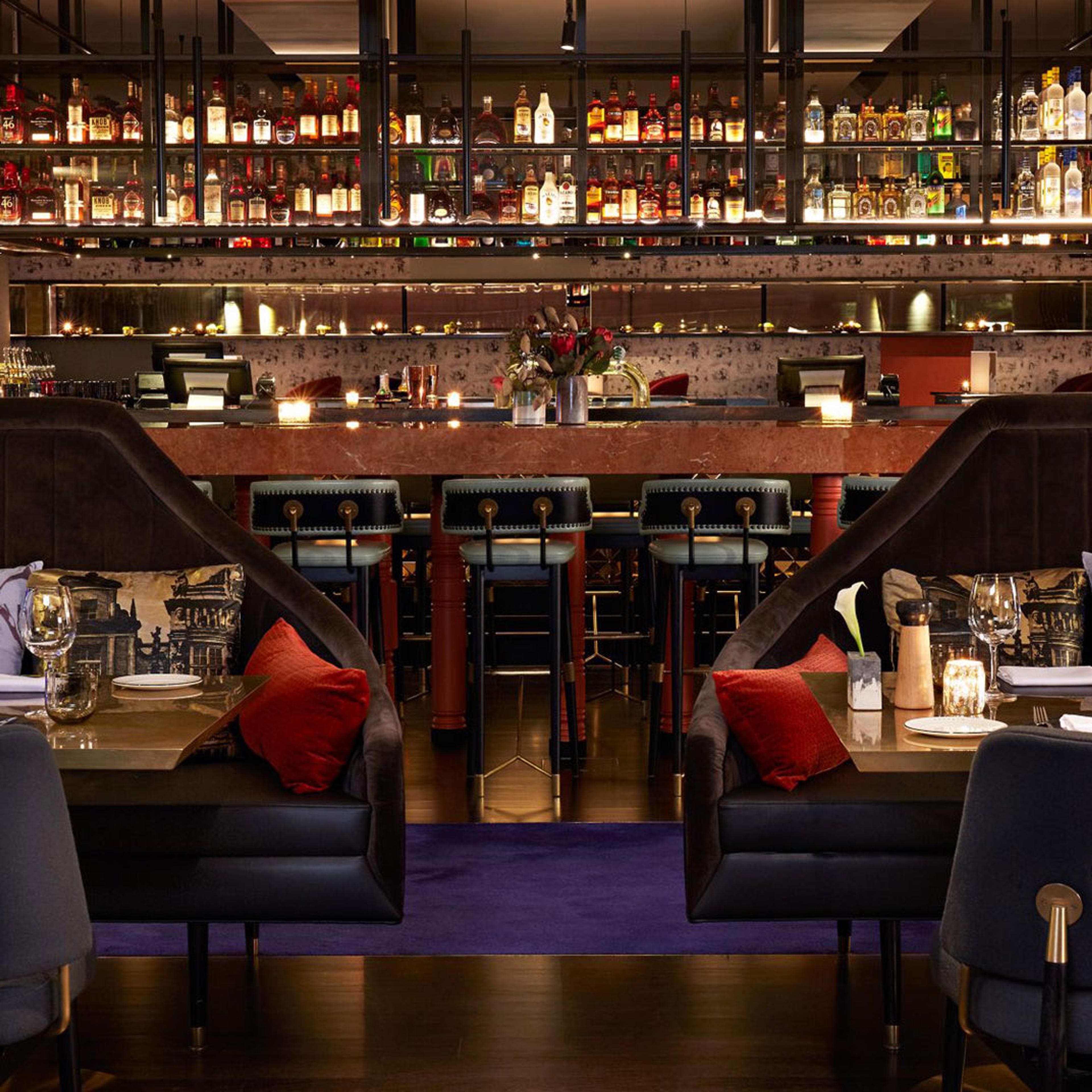 A dim bar with red banquettes and low lamps