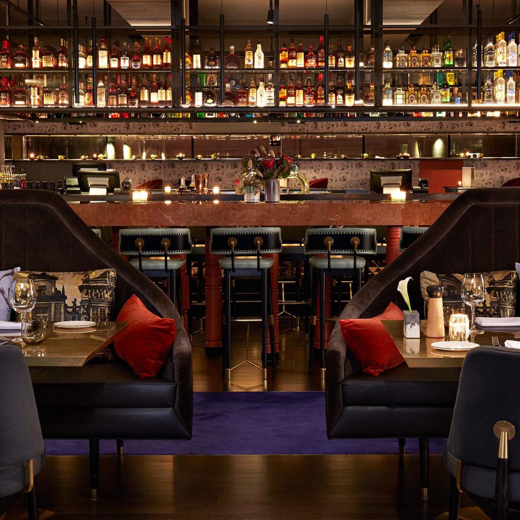 A dim bar with red banquettes and low lamps