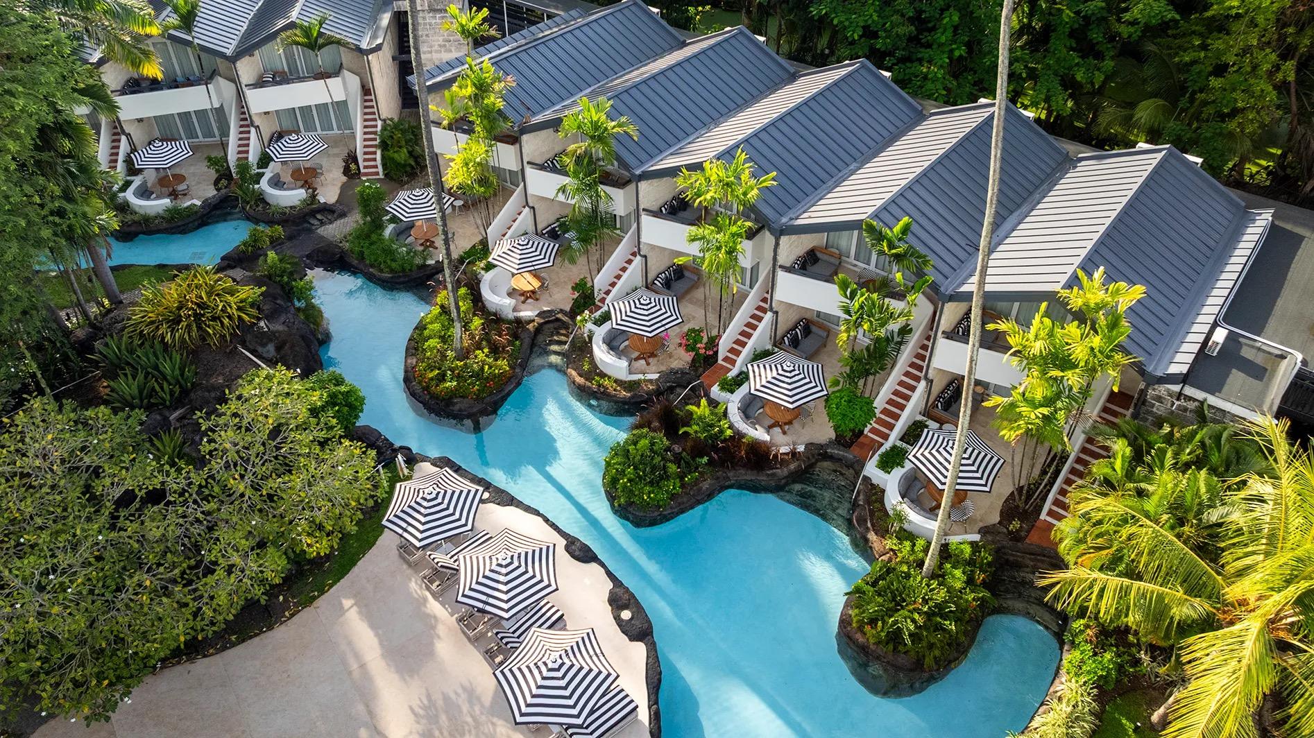 A lagoon pool winding past the ground-floor rooms, each with steps down to the water and a striped parasol