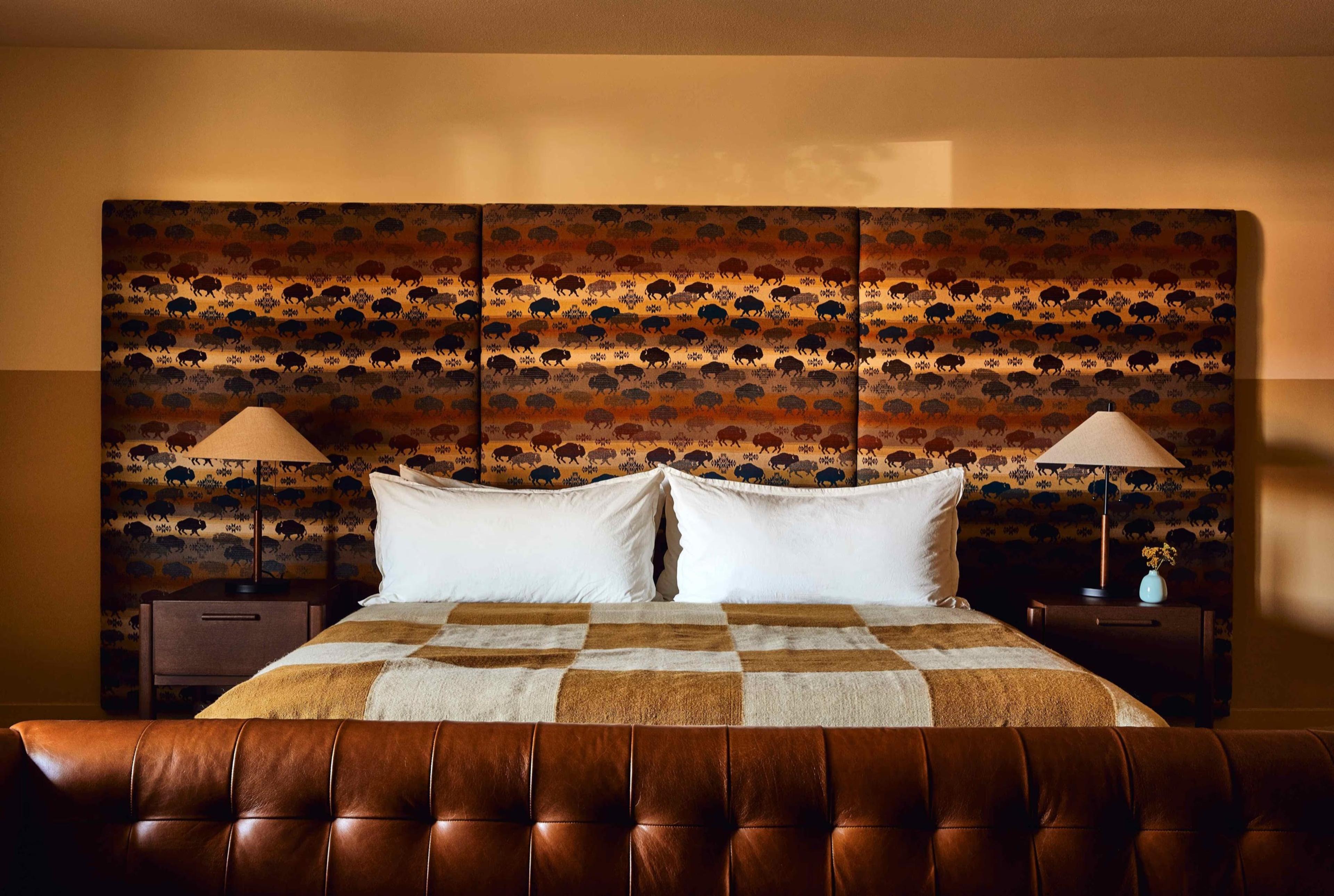 A bed with white pillows and a brown and beige checkered blanket, flanked by lit nightstands under a bison-patterned headboard.