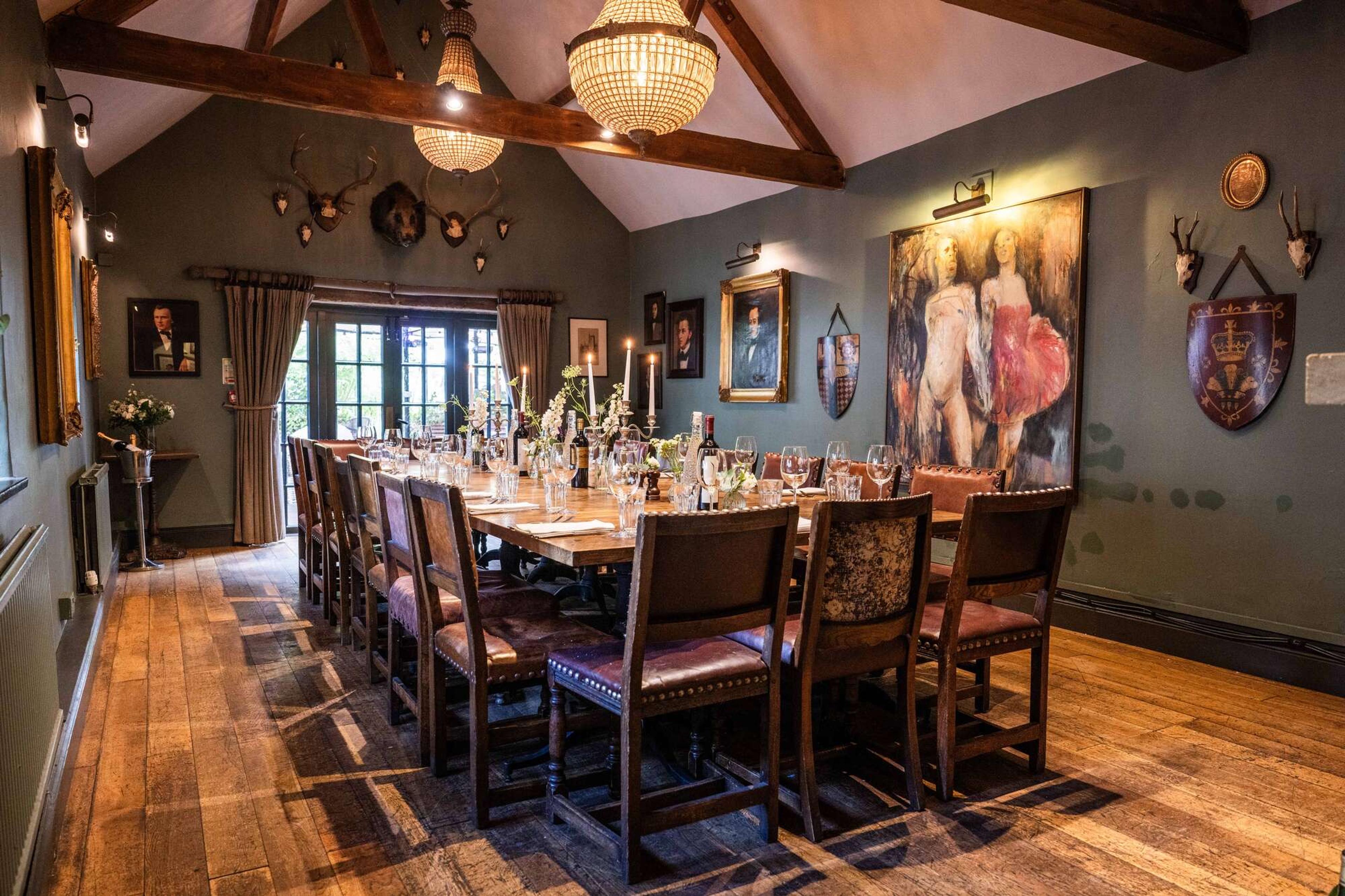 A long dining table set for a group under exposed timber beams, with taxidermy, oil paintings and candlesticks on the walls and table.