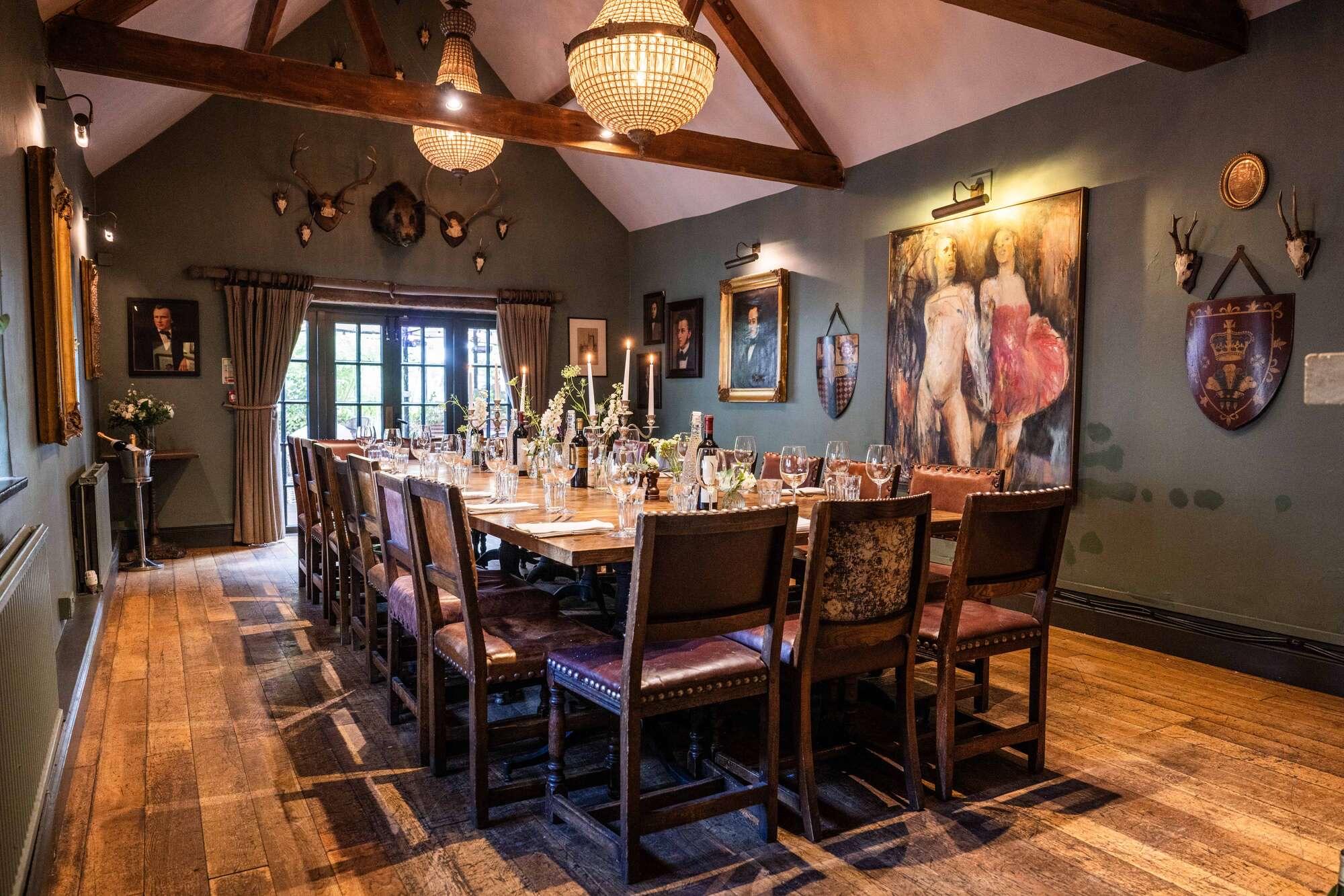 A long dining table set for a group under exposed timber beams, with taxidermy, oil paintings and candlesticks on the walls and table.