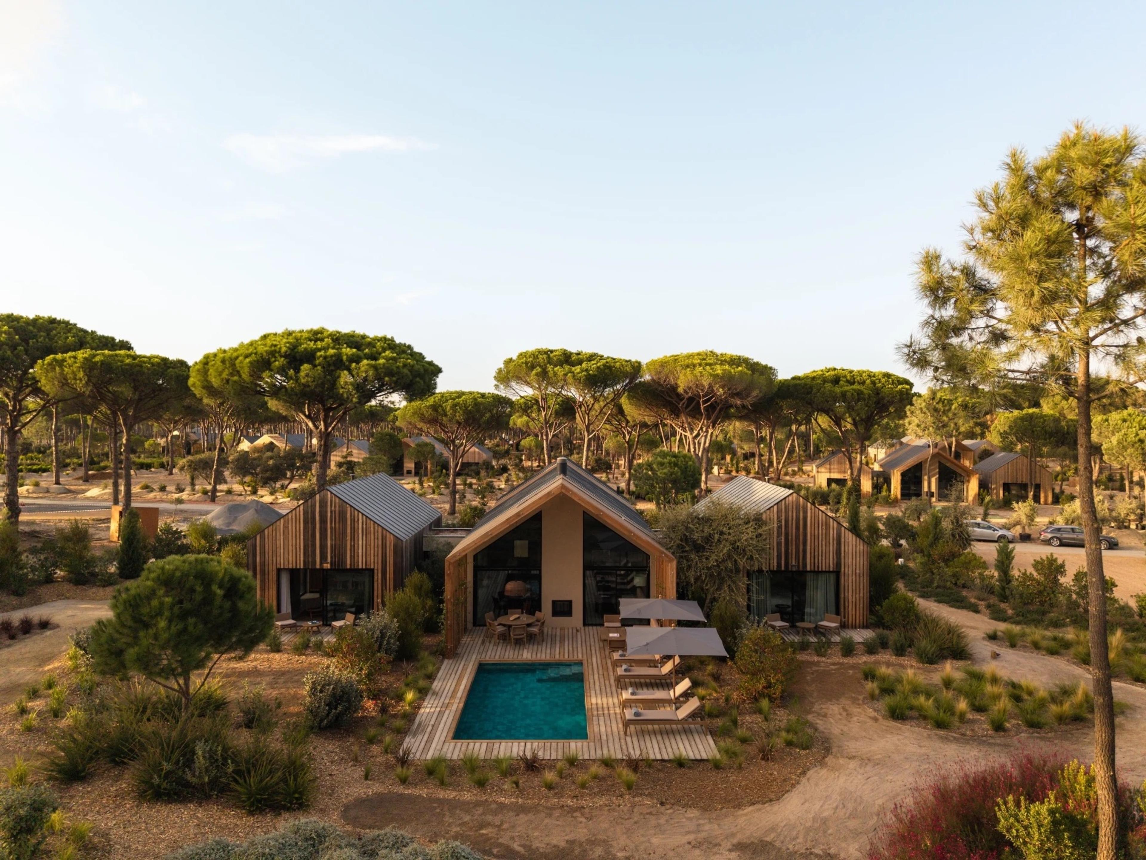 An aerial view of a single-storey villa with a private pool, sun loungers and umbrellas, ringed by pine trees.