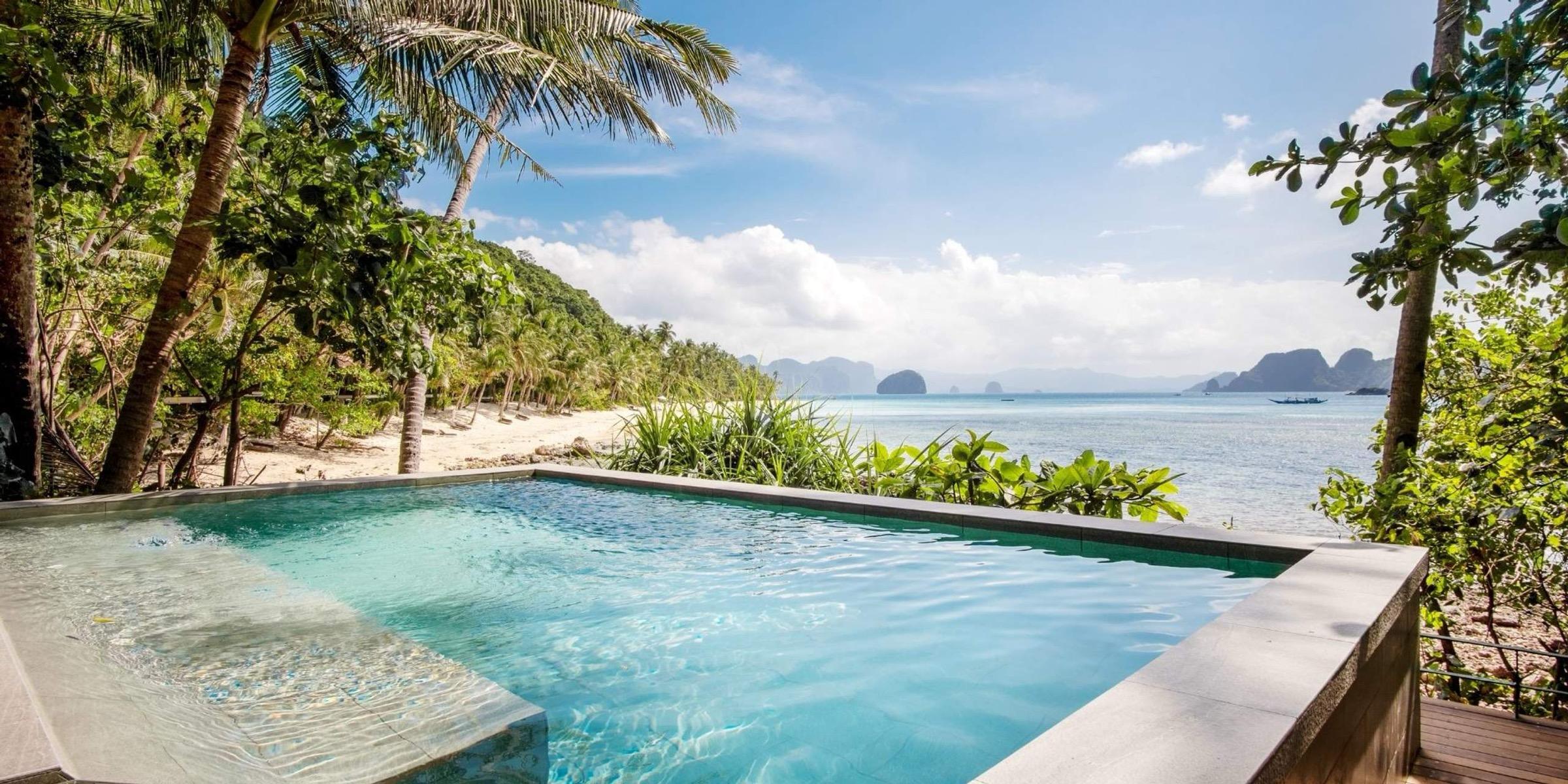 An infinity pool at the edge of the beach, palms on one side and islands across the bay.