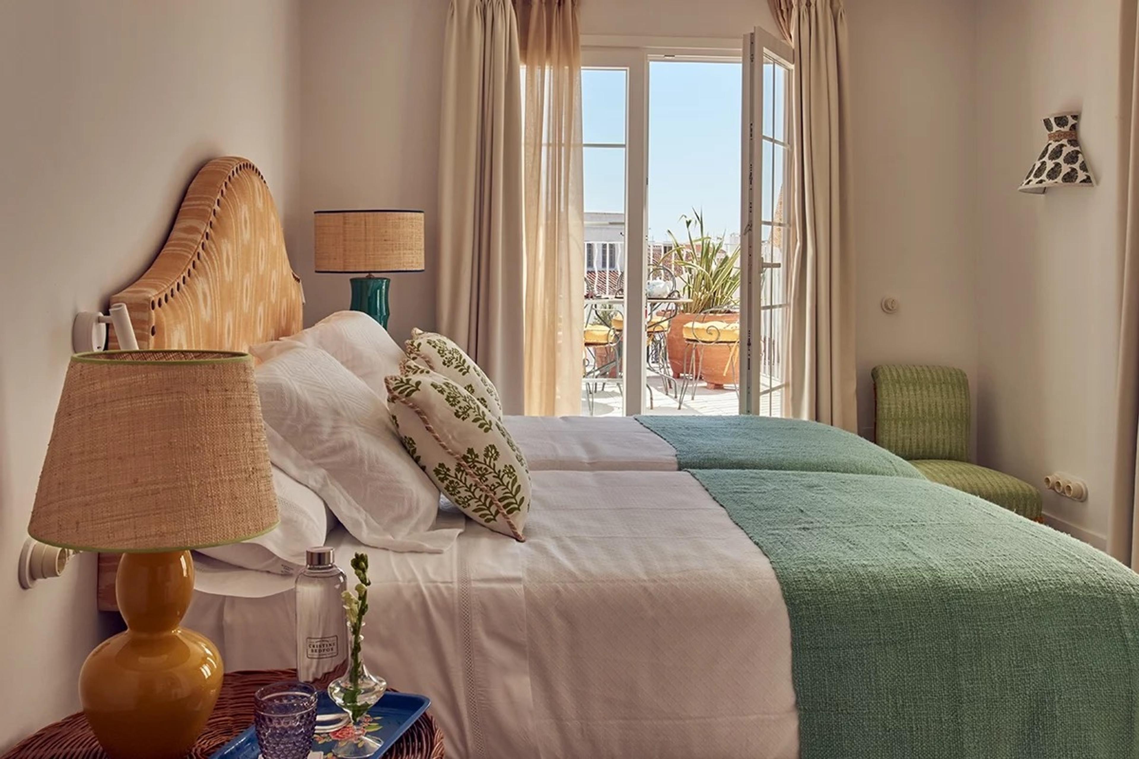 A twin-bed room in green and cream, with patterned cushions and French doors open onto a balcony.